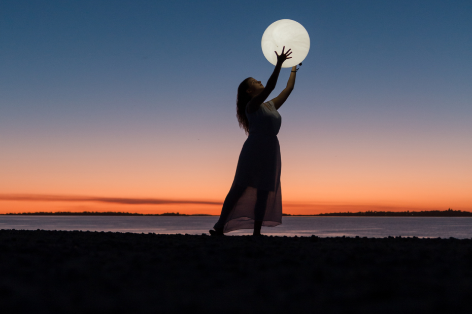Vrouw bij zonsondergang die de volle maan pakt